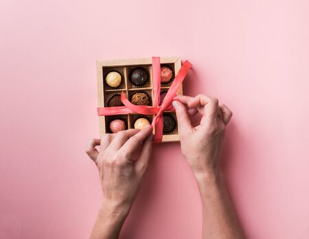 A woman unties a bow opens a box of chocolates. Set of different chocolates in a paper box in female hands.の写真素材