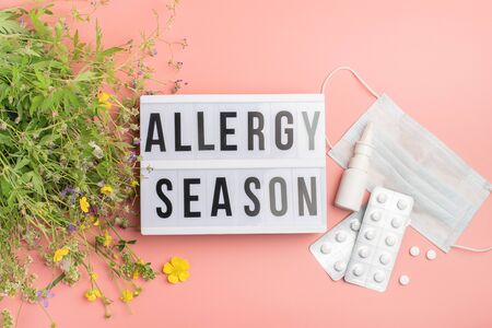 The concept combating preventing seasonal allergies. Fresh flowers medical mask pills drops medicine pink background.の写真素材