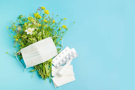The concept of combating preventing seasonal allergies. Fresh flowers protective medical mask pills drops of medicine on a blue background. Horizontal frame copy spaceの写真素材