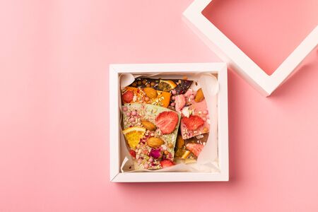 Chocolate pieces of various color toppings in a box on pink background. The concept of a festive dessert. Copy spaceの写真素材