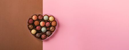 Chocolate candies truffle made of different colored chocolate in a heart shape box on a pink...