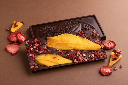 Chocolate dark Belgian bar with the addition of fruit slices of strawberry mango on a brown...