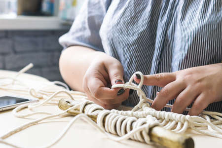 Female hands weave macrame the home workshop. Boho lifestyle. Hobby hobby concept. Selective focus...