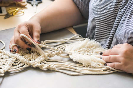 Female hands weave macrame the home workshop. Boho lifestyle. Hobby hobby concept. Selective focus horizontal frame.の写真素材