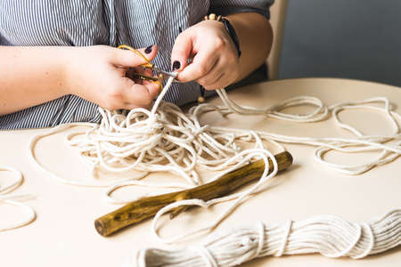 Female hands weave macrame in the home workshop. Boho lifestyle. Hobby hobby concept. Selective...