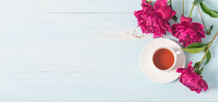 Red pink peonies tea cup on a blue wooden background. Horizontal frame copy space for text design. Top view flat layoutの写真素材