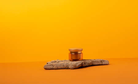 A jar of cream bottle on a podium made of natural wood materials on a bright orange background. Template for advertising cosmetics concept minimalism copy spaceの写真素材