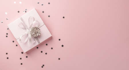 Festive box with a shiny ribbon bow on a pastel pink background with sequins confetti. Flat top view. Copy space bannerの写真素材