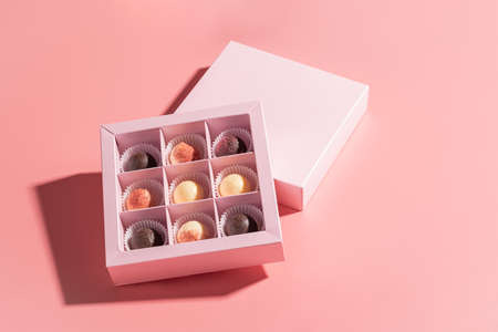Chocolate candies in a festive box on a pink background. Holiday concept. Minimalism food dessert. Horizontal frame copy space. Hard shadow isometricの写真素材