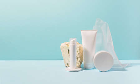 Group of cosmetic tubes of white color bottles on a modern abstract podium of natural materials on a pastel blue background. Cosmetics presentation advertising templateの写真素材