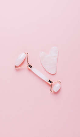 Facial massage set roller massager and gua sha scraper for face care on pastel pink background. Lifting and toning fitness for the face at home. Vertical frame copy spaceの写真素材