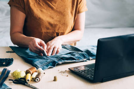 A woman is engaged in online training and looks at sewing lessons on a laptop. Concept of trendy online learning taking courses at home. Homemade needlework hobbyの写真素材
