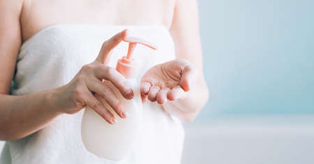 Female hands pumping out cream, lotion, liquid soap from a white bottle, selective focus. Skin body care conceptの写真素材