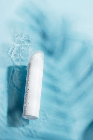 White bottle for skin care, cream gel, serum, spa, cosmetic product on a blue background of pool...