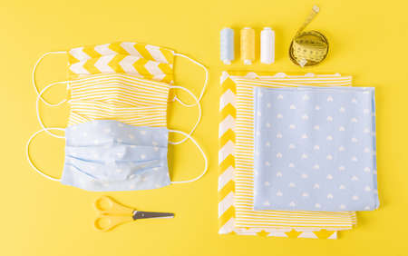 Eco-friendly reusable cloth face shield and sewing accessories on top yellow background. Homemade...