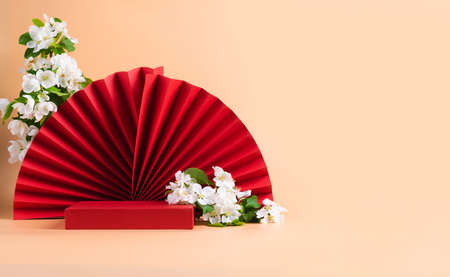 Red podium paper oriental fan flowering branch with buds pink pastel backgroundの写真素材