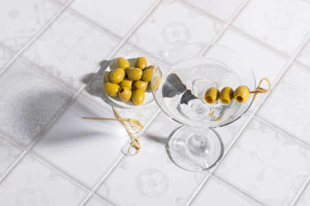Martini cocktail with olives on the tiled table. An alcoholic classic drink with ice in an elegant...