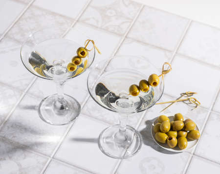 Martini cocktail with olives on the tiled table. An alcoholic classic drink with ice in an elegant glassの写真素材