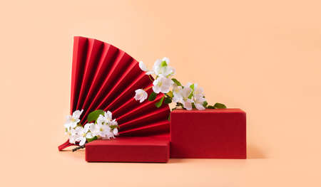 Red podium paper oriental fan flowering branch with buds pink pastel background. Abstract fashion podium for advertising cosmetics products. Front view copy spaceの写真素材