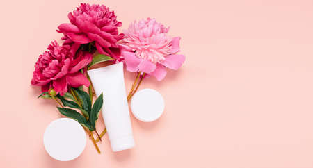 Cosmetic products cream gel shampoo balm in various bottles on a pink background with fresh flowers peoniesの写真素材