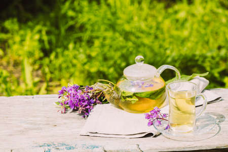 Tea with fresh lemon balm summer herbs clover leaves in glass cup and teapot on wooden rustic backgroundの写真素材