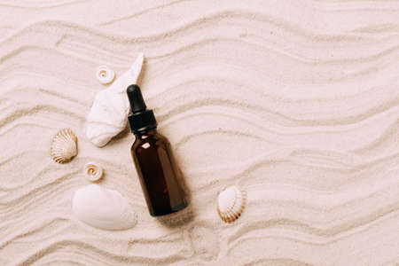 Glass bottle with essential oil serum cosmetic product background of seashells beach sand, product presentationの写真素材
