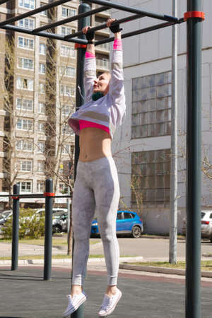 Young woman fashionable sportswear with headphones performs strength fitness exercises on a...