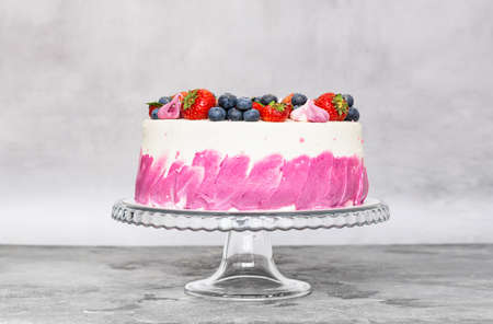 Delicate cake garnished with fresh strawberries blueberries on a gray plain background. Festive...