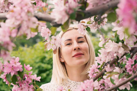 Young woman among the blossoming trees. Spring nature park or garden, flowering trees. Concept spring woman healthの写真素材