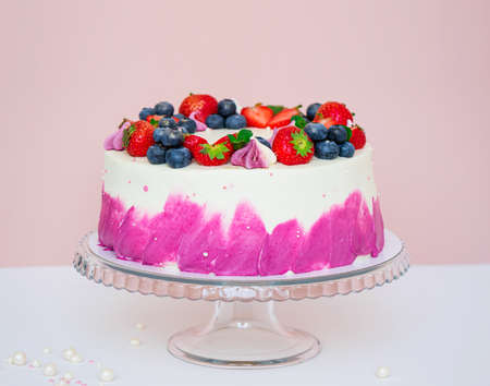 Delicate cake decorated with fresh berries, strawberries and blueberries on a light plain backgroundの写真素材