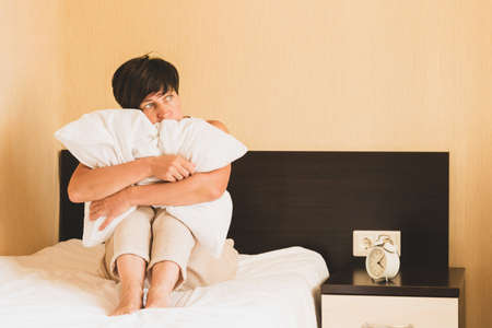A middle-aged woman sits in bed hugging a pillow. Womens health depression sleep problems sadness loneliness.の写真素材