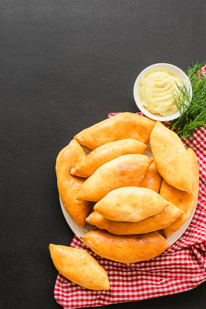 Small pies with a crispy golden crust of potato filling lie on a plate on a black background. Homemade country bakingの写真素材