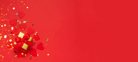 Gift with a red bow on a red background with glitter hearts and confetti. Festive flat composition...