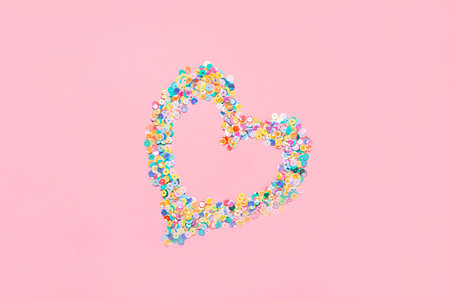 Heart made of multicolored sequins confetti on pink background. Flat festive composition copy spaceの写真素材