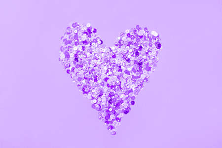 Heart made of multicolored sequins confetti on violet very peri background. Flat festive composition...