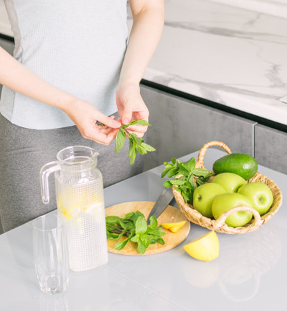 Woman in sportswear makes detox drink with lemon mint in kitchen at home. Rejuvenating invigorating water lemon,の写真素材