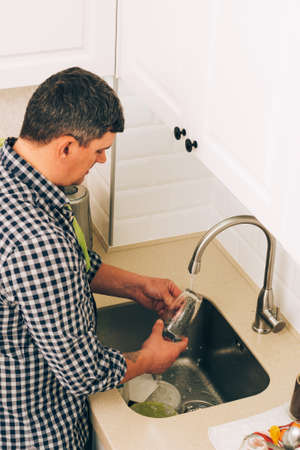 A man wash dishes with detergent and a sponge under running clean water in the sink at home. Lifestyleの写真素材