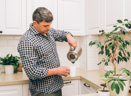 A man pours hot water from a kettle into a white mug to make tea or coffee. Positive lifestyleの写真素材