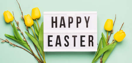 Festive spring composition yellow tulips twigs of fluffy willow and board with the text Happy Easterの写真素材