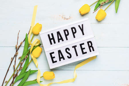 Festive spring composition yellow tulips twigs of fluffy willow and board with the text Happy Easterの写真素材