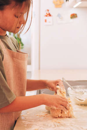 Cute teenage girl in kitchen apron prepares and kneads products for making dough for baking