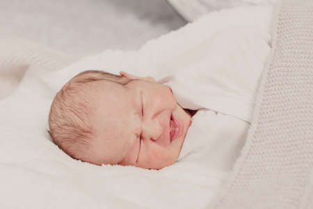 Newborn baby in a wrap on a white blanket, emotional portrait of a 7 days old babyの写真素材