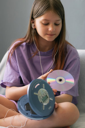 A teenage girl in a lilac T-shirt lies on a bed and listens to music on CD disk