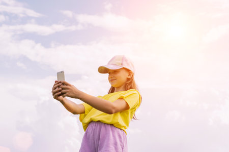 A preteen girl takes a selfie on a mobile phone against a blue sky. Horizontal frame, copy spaceの写真素材