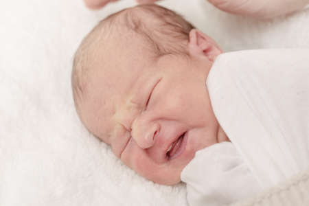 Newborn baby in a wrap on a white blanket, emotional portrait of a 7 days old baby