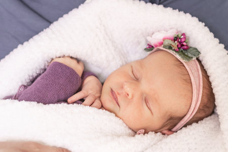 Sleeping newborn baby girl wrapped in a white fluffy blanket in the arms of the parents, first monthの写真素材