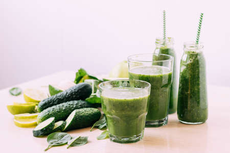 Green vegetable fruit smoothie in various glasses portion bottles on kitchen table, light backgroundの写真素材