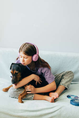 Happy teenage girl in lilac t-shirt in pink headphones listens to music and has fun playing with dogの写真素材