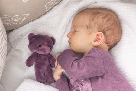 Cute newborn baby girl sleeps at home in her crib with her favorite toy, the first month of lifeの写真素材