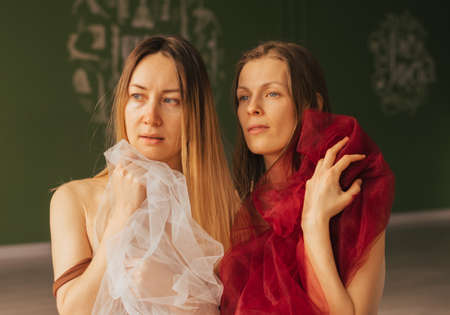 Two adult Women with blond long hair and a red transparent cloth in their hands touch each otherの写真素材